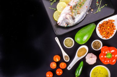 Fresh raw gilthead fishes with lemon, herbs, salt on black background. Healthy food concept. Food frame. Free space for your text.