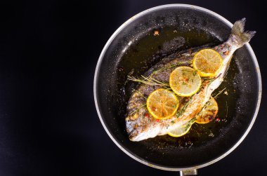Roasted gilthead fishes with lemon, herbs, salt on black background. Healthy food concept. Food frame. Free space for your text.