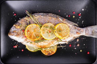 Roasted gilthead fishes with lemon, herbs, salt on black background. Healthy food concept. Food frame. Free space for your text.