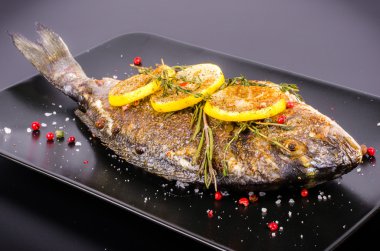 Roasted gilthead fishes with lemon, herbs, salt on black background. Healthy food concept. Food frame. Free space for your text.