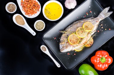 Roasted gilthead fishes with lemon, herbs, salt on black background. Healthy food concept. Food frame. Free space for your text.