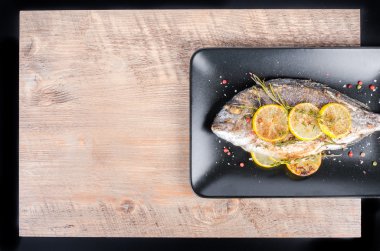 Roasted gilthead fishes with lemon, herbs, salt on wooden background. Healthy food concept. Food frame. Free space for your text.