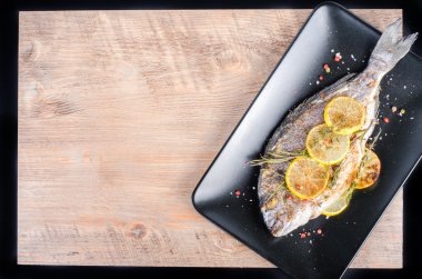 Roasted gilthead fishes with lemon, herbs, salt on wooden background. Healthy food concept. Food frame. Free space for your text.