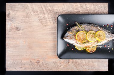 Roasted gilthead fishes with lemon, herbs, salt on wooden background. Healthy food concept. Food frame. Free space for your text.