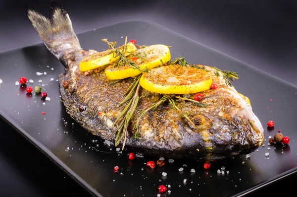 Roasted gilthead fishes with lemon, herbs, salt on black background. Healthy food concept. Food frame. Free space for your text. — Zdjęcie stockowe