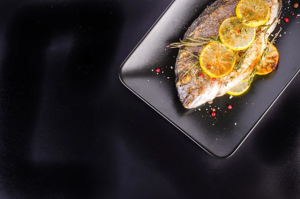 Roasted gilthead fishes with lemon, herbs, salt on black background. Healthy food concept. Food frame. Free space for your text. — Stockfoto
