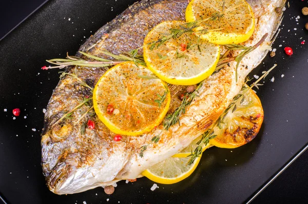 Roasted gilthead fishes with lemon, herbs, salt on black background. Healthy food concept. Food frame. Free space for your text. — Stockfoto