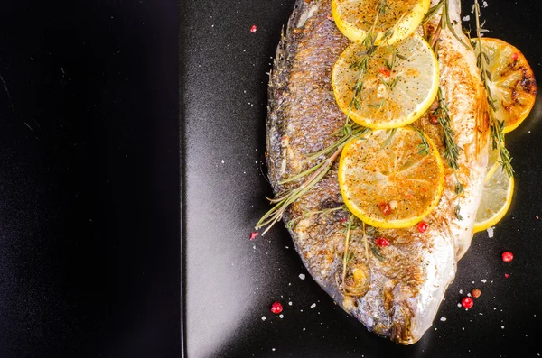 Roasted gilthead fishes with lemon, herbs, salt on black background. Healthy food concept. Food frame. Free space for your text. — 스톡 사진