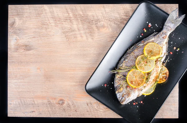 Roasted gilthead fishes with lemon, herbs, salt on wooden background. Healthy food concept. Food frame. Free space for your text. — Stockfoto