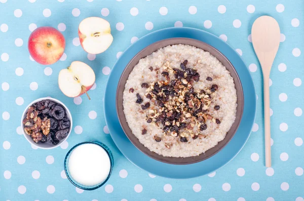 Desayuno listo. Un tazón de gachas de cebada con aceite de coco, leche vegetariana, nueces, pasas, canela sobre mantel de lunares azules, cuchara, manzana, vaso de leche vegetariana. Espacio libre para tu texto . —  Fotos de Stock