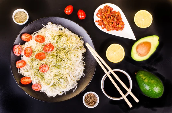 Tagliatelle di riso cinese con pesto, pomodorini ciliegia, avocado, salsa di soia, limone e spezie su sfondo nero . — Foto Stock