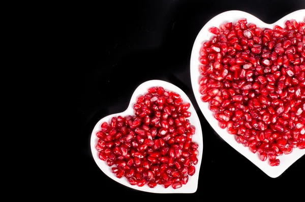 Two white heart shaped plate full of fresh ripe juicy pomegranate seeds on black background. Free space for your text. — Zdjęcie stockowe