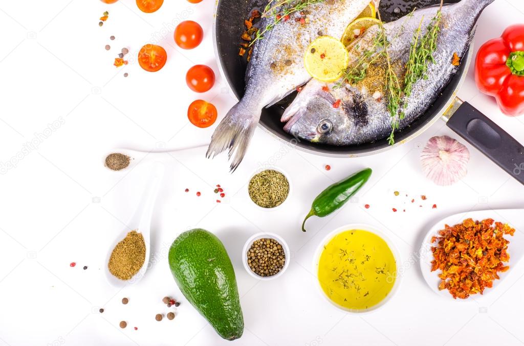 Fresh raw gilthead fishes with lemon, herbs, salt on white background. Healthy food concept. Food frame