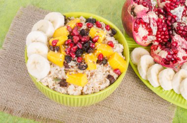 Oatmeal with mango, banana, seeds of pomegranate, raisins, dried fruits and sesame on canvas and green background. Healthy vegetarian breakfast.  clipart