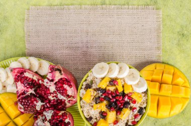 Oatmeal with mango, banana, seeds of pomegranate, raisins, dried fruits and sesame on canvas and green background. Healthy vegetarian breakfast. Free space for your text.