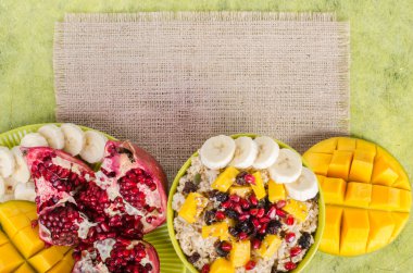 Oatmeal with mango, banana, seeds of pomegranate, raisins, dried fruits and sesame on canvas and green background. Healthy vegetarian breakfast. Free space for your text. clipart