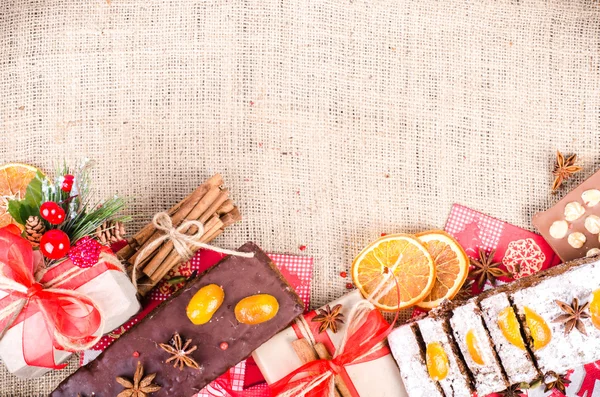 Chocolate spices cake, star anise and dried fruits, packed gifts with red tapes on sackcloth, canvas. Sweet frame. Free space for your text.