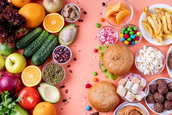 Fruit and vegetables vs sweets and fast food top view flat lay on orange background