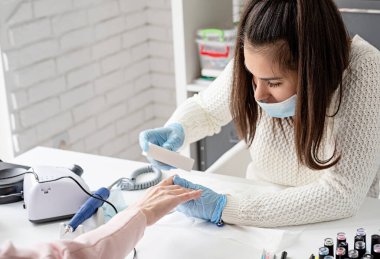 Manikür ve pedikür salonu, covid-19 ve sosyal mesafe. Bir müşterinin manikür ustası ve eldiven parlatıcı tırnakları