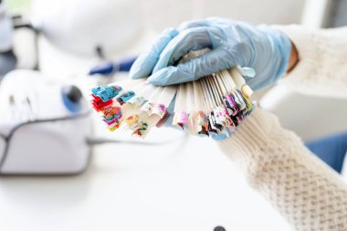 Manikür ustası manikürcüde çalışıyor. Elinde renkli ojeli çeşitli plastik tırnak uçları var.