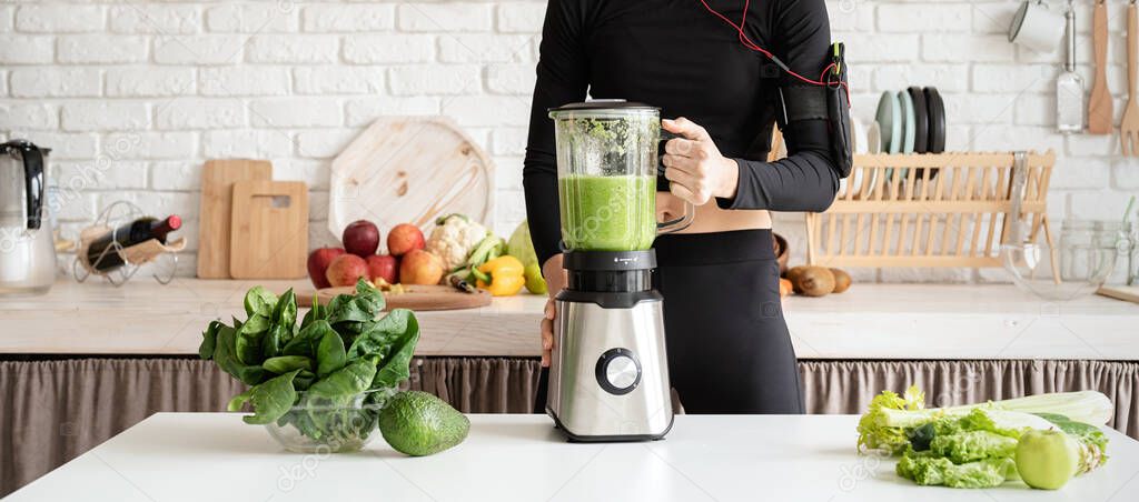 Healthy eating, dieting concept. Young blond smiling woman making green smoothie at home kitchen