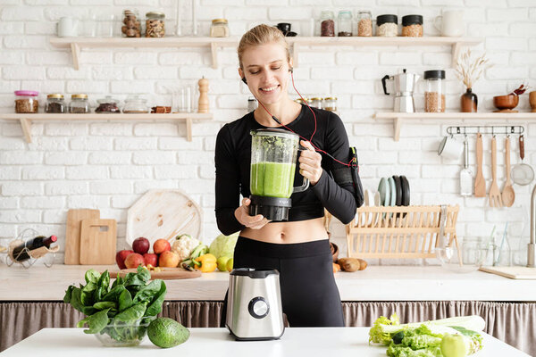 Healthy eating, dieting concept. Young blond smiling woman making green smoothie at home kitchen