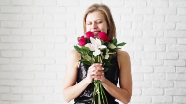 Beyaz tuğla duvar arkasında çiçek kokusu alan genç pozitif bir kadın.