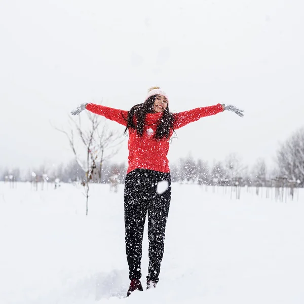 Jovem morena em camisola vermelha brincando com neve no parque — Fotografia de Stock