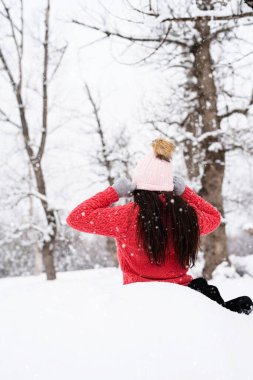 Kış mevsimi. Kar yağışı altında kar parkında oturan esmer kadın şapkasını takıyor.