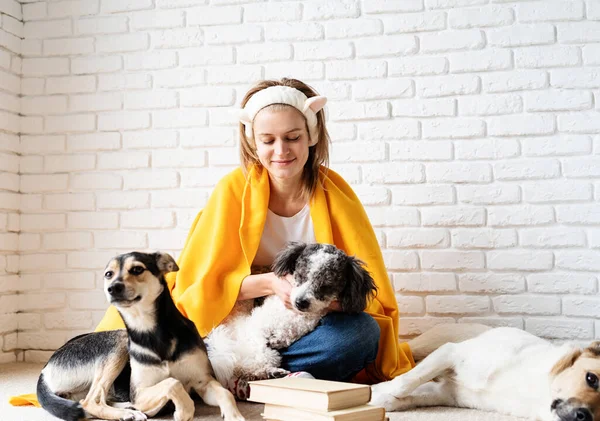 Pet care. Funny smiling young woman in yellow plaid sitting with her dogs reading a book