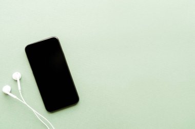 Yeşil arka planda boş ekran kulaklıkları olan akıllı telefonun üst görünümü