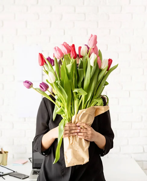 Küçük işletme konsepti. Genç, kendine güvenen esmer iş kadınının portresi masanın yanında duruyor taze lale buketiyle.