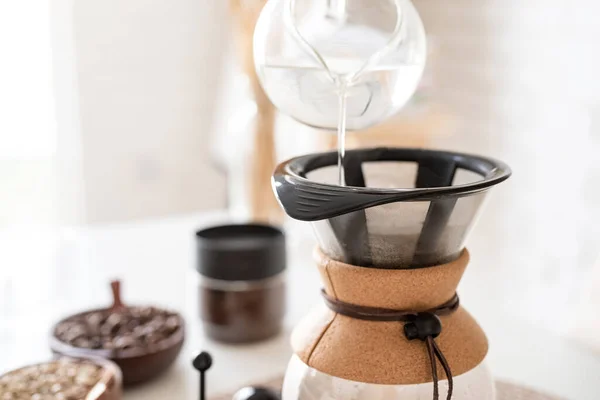 Alternative coffee brewing. Young woman brewing coffee in coffee pot standing at the white table with various stuff for alternative coffee brewing, pouring hot water into the filter