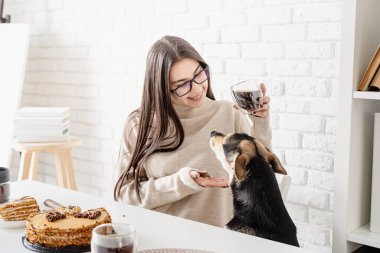 Alternatif kahve demleniyor. Genç esmer kadın sıcak siyah kahve içiyor beyaz masada oturuyor, köpekle oynuyor.