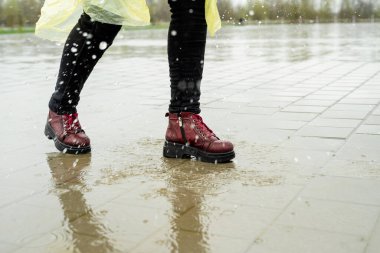 Yağmurlu havada asfaltta koşan bir kadın. Su birikintilerinde süzülen ayaklar ve ayakkabılar.