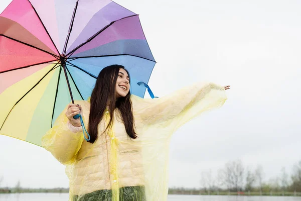 Beautiful brunette woman holding colorful umbrella out in the rain