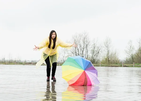 Funny woman catching colorful umbrella outdoors in the rain