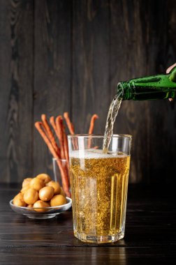 Bira şişeden cama dökülüyor, siyah ahşap arka plan.