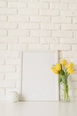 Cam bir vazoda sarı lale buketi ve beyaz tuğla duvar zemininde boş fotoğraf çerçevesi. Tasarımı düzenle
