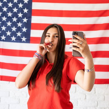 Amerika 'nın bağımsızlık günü. 4 Temmuz kutlu olsun. Gürültücüsü olan güzel bir kadın Amerikan bayrağının arka planında selfie çekiyor.