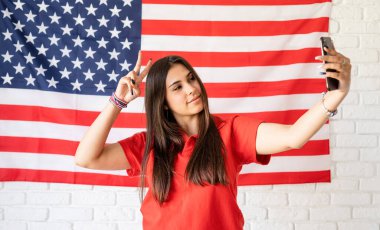 Amerika 'nın bağımsızlık günü. 4 Temmuz kutlu olsun. Güzel bir kadın Amerikan bayrağının arka planında selfie çekiyor.