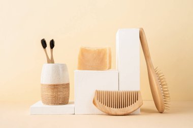 Doğal organik öz bakım ürünleri. Beyaz podyumlarda el yapımı sabun, ahşap fırça ve bambu diş fırçası. Bej arka planda spa aksesuarları yaratıcı sanat kompozisyonu