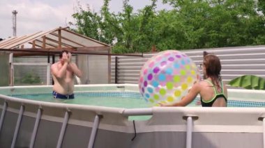Mutlu genç adam ve kadın bahçede yüzme havuzunda topla oynuyorlar.