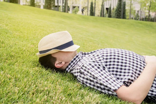 公園の草の上に座って 離れて見て夏の帽子の若い思慮深い男 — ストック写真
