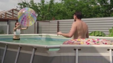 Mutlu genç adam ve kadın bahçede yüzme havuzunda topla oynuyorlar.