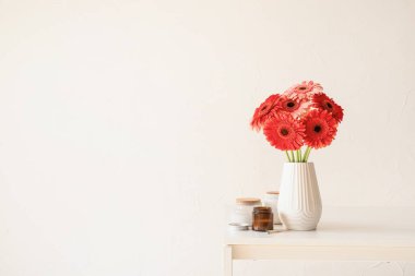 Kırmızı ve pembe gerbera papatyaları mutfak masasının üzerinde beyaz vazolar içinde mumlar, minimum stil, kopyalama alanı
