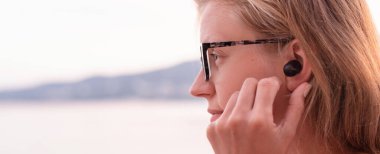 Teknoloji konsepti. Kablosuz kulaklık kullanan bir kadın, arka planda deniz kenarı, afiş.