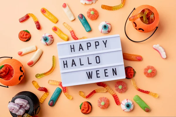 Halloween concept. Halloween party decorations with lightbox with words Happy Halloween, sweets, pumpkins top view flat lay on orange background