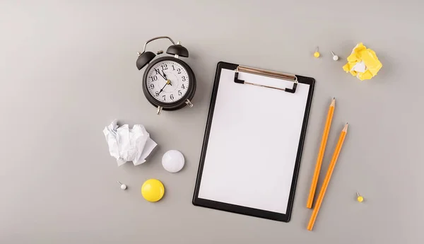 Papel en blanco en el portapapeles, despertador blanco y papelería vista superior sobre fondo gris — Foto de Stock