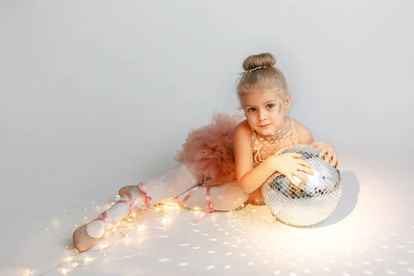 Küçük dansçı kız. Sirk disko topuyla balerin. Sirk aydınlatması. Beyaz arka planda çelenk. Boşluğu kopyala.